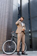 © LIGHTFIELD STUDIOS - low angle view of businessman talking on smartphone and holding paper cup near bicycle and building