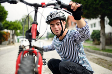 Portrait of down syndrome adult man with bicycle standing outdoors on street.