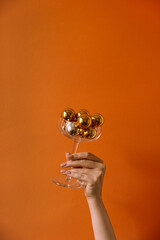 Poster - Female hand holding wineglass with gold Christmas baubles. Christmas / New year concept. Minimal background.