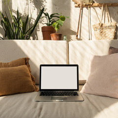 Wall Mural - laptop with blank screen on comfortable sofa in warm sunlight shadows. minimal boho styled interior 