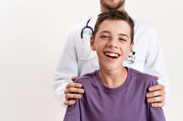 Cropped shot of teenaged disabled boy with cerebral palsy smiling at camera, standing with his male doctor isolated over white background