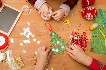 hands mom and little daughter make crafts Christmas toys on a Christmas tree