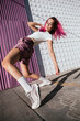 © VISTA by Westend61 - Young woman with dyed red hair dancing in front of purple wall in the city