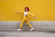 © VISTA by Westend61 - Energetic young woman in yellow suit running and jumping in front of yellow wall