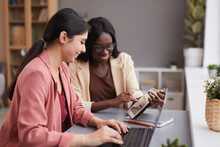 Side View Portrait Of Two Ethnic Businesswomen Using Digital Tablet During Meeting While Managing Successful Business Together, Copy Space