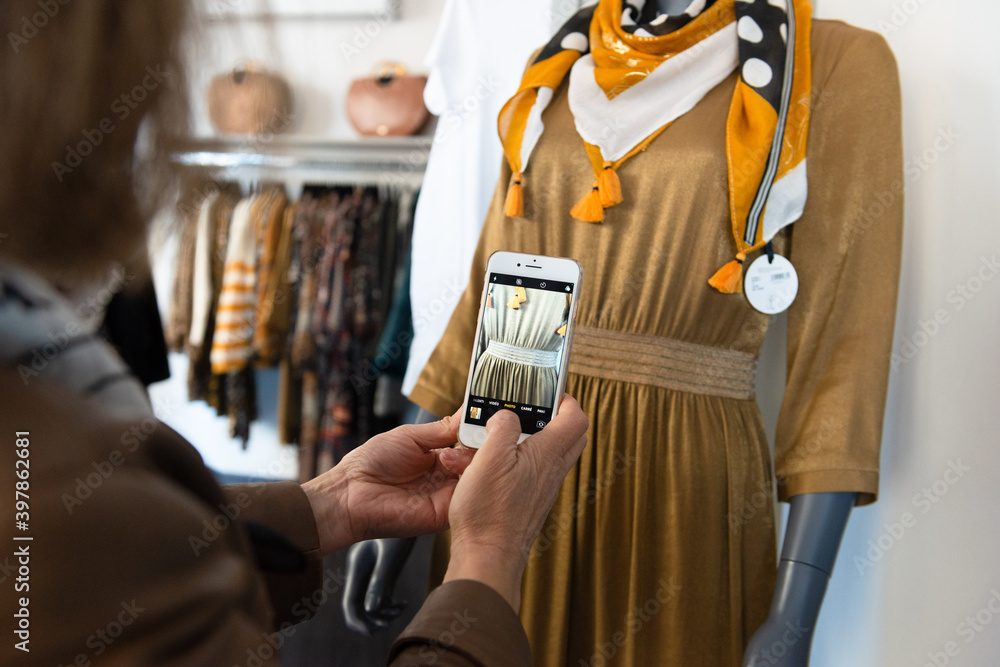 Gros plan des mains d'une commerçante photographiant un détail d'un vêtement pour femme sur le mannequin de sa boutique - obrazy, fototapety, plakaty 