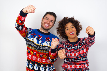 Young couple wearing Christmas sweater standing against white wall  imagine steering wheel helm rudder passing driving exam good mood fast speed