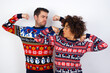 © Roquillo - Young couple wearing Christmas sweater standing against white wall showing arms muscles smiling proud. Fitness concept.