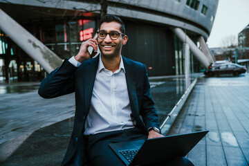 Smiling mixed race businessman chatting on mobile device holding laptop