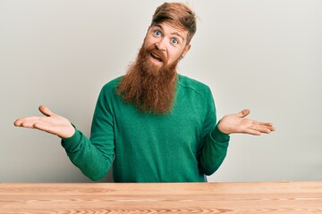 Sticker - Young irish redhead man wearing casual clothes sitting on the table clueless and confused expression with arms and hands raised. doubt concept.