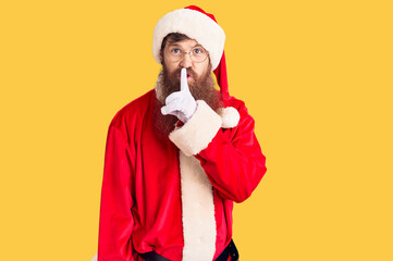 Wall Mural - Handsome young red head man with long beard wearing santa claus costume asking to be quiet with finger on lips. silence and secret concept.