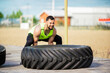 © Georgii - Sports guy training with tire, workout outdoor. Male in stylish sportswear exercising with weight