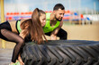 © Georgii - Athletic couple in stylish sportswear lifting tire, powerful pair workout outdoor