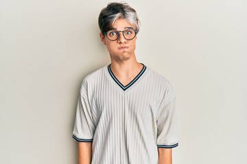 Sticker - Young hispanic man wearing casual clothes and glasses puffing cheeks with funny face. mouth inflated with air, crazy expression.