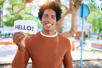 Wall Mural - Young handsome african american man smiling happy. Standing with smile on face holding hello message paper at town street.