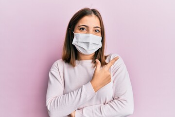 Poster - Young beautiful woman wearing medical mask smiling cheerful pointing with hand and finger up to the side