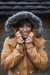 Winter portrait of a beautiful woman smiling with her fur hood on while holding the neckline of her yellow jacket