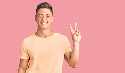 Poster - Young handsome man wearing casual clothes showing and pointing up with fingers number two while smiling confident and happy.