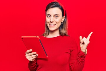 Young beautiful woman holding touchpad smiling happy pointing with hand and finger to the side