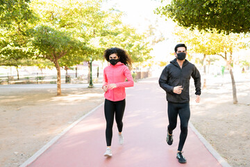  Full length of a fit couple with face masks running together outdoors