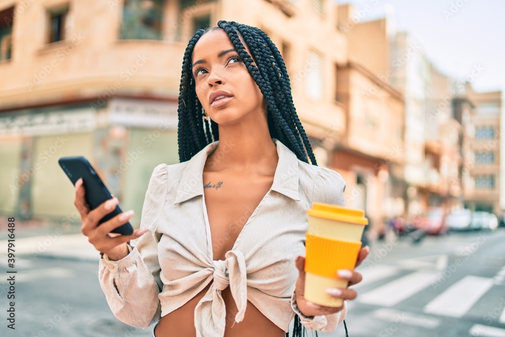 Young african american woman with serious expression using smartphone and drinking coffee at the city.