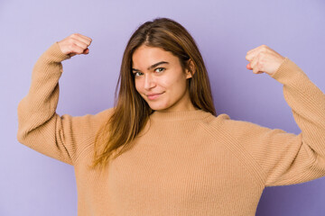 Young skinny caucasian girl teenager on purple background showing strength gesture with arms, symbol of feminine power