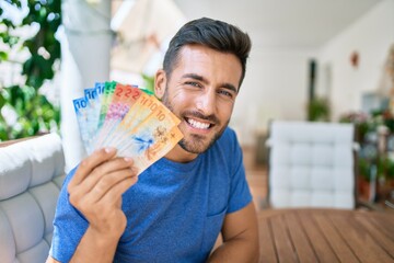 Poster - Young hispanic man smiling happy holding swiss franc banknotes at the terrace.