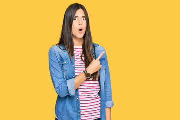 Sticker - Young brunette woman wearing casual clothes surprised pointing with finger to the side, open mouth amazed expression.