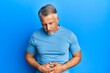 © Krakenimages.com - Middle age grey-haired man wearing casual clothes with hand on stomach because indigestion, painful illness feeling unwell. ache concept.
