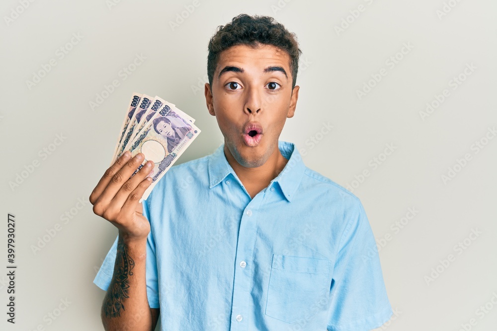 Young handsome african american man holding 5000 japanese yen banknotes scared and amazed with open mouth for surprise, disbelief face