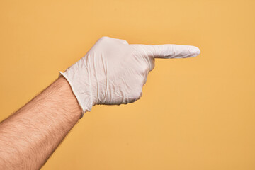 Hand of caucasian young man with medical glove over isolated yellow background pointing with index finger to the side, suggesting and selecting a choice