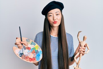 Poster - Young chinese woman wearing artist look with beret holding manikin looking at the camera blowing a kiss being lovely and sexy. love expression.