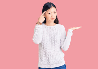 Sticker - Young beautiful chinese woman wearing casual sweater confused and annoyed with open palm showing copy space and pointing finger to forehead. think about it.