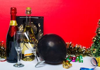 Champagne bottles with two glasses, black latex balloon and multi-colored tinsel on red background. Celebration theme with champagne still life. Template for postcards for Christmas and New Year 2021.