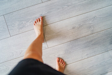 Top view on barefoot female legs walking on laminated wooden floor in day - feet of unknown woman standing at home - close up high angle view copy space - freedom and leisure concept