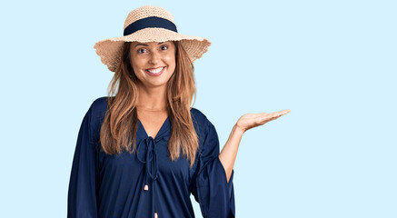 Sticker - Middle age hispanic woman wearing summer hat smiling cheerful presenting and pointing with palm of hand looking at the camera.