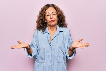 Poster - Middle age beautiful woman wearing casual denim shirt standing over pink background clueless and confused with open arms, no idea concept.