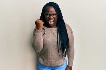 Sticker - Young black woman with braids wearing casual clothes and glasses angry and mad raising fist frustrated and furious while shouting with anger. rage and aggressive concept.