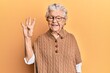 © Krakenimages.com - Senior grey-haired woman wearing casual clothes and glasses showing and pointing up with fingers number four while smiling confident and happy.
