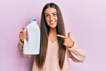 Wall Mural - Beautiful hispanic woman holding laundry detergent bottle smiling happy pointing with hand and finger