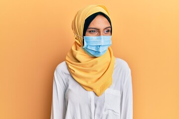 Wall Mural - Young brunette arab woman wearing traditional islamic hijab and medical mask looking away to side with smile on face, natural expression. laughing confident.