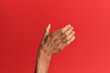 Hand of hispanic man over red isolated background holding invisible object, empty hand doing clipping and grabbing gesture