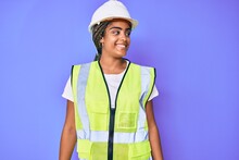 Young African American Woman With Braids Wearing Safety Helmet And Reflective Jacket Looking Away To Side With Smile On Face, Natural Expression. Laughing Confident.