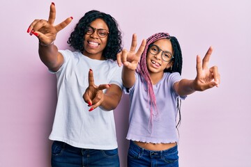 Sticker - Beautiful african american mother and daughter wearing casual clothes and glasses smiling with tongue out showing fingers of both hands doing victory sign. number two.