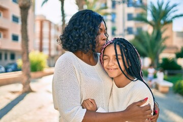 Poster - Beautiful african american mother and daughter kissing and hugging. Standing with smile on face standing at the park.