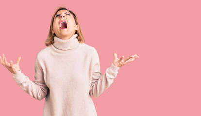 Wall Mural - Young blonde woman wearing casual clothes crazy and mad shouting and yelling with aggressive expression and arms raised. frustration concept.