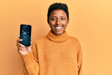 Wall Mural - Young african american girl holding broken smartphone showing cracked screen looking positive and happy standing and smiling with a confident smile showing teeth