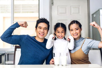 Portrait of enjoy happy love asian family father and mother  with little asian girl smiling and having breakfast drinking and hold glasses of milk at table in kitchen