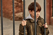 street boy stands behind bars, looks at people passing by, wants to live happily, depressed, need shelter