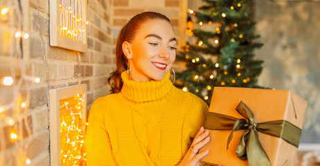 Wall Mural - Beautiful cheerful happy young girl with christmas gifts on the background of a new year tree at home